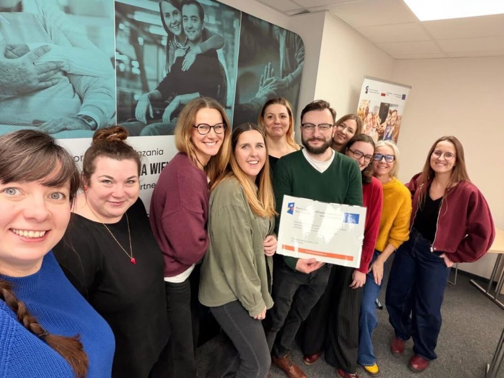 Grupa osób, uśmiechnięta. Osoby ustawiły się do zdjęcia. Pozują z kartką wskazującą na rodzaj omawianych podczas spotkania zagadnień.