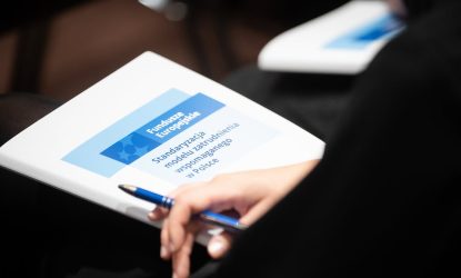 Osoba siedząca tyłem trzyma na kolanach teczkę z nazwą projektu